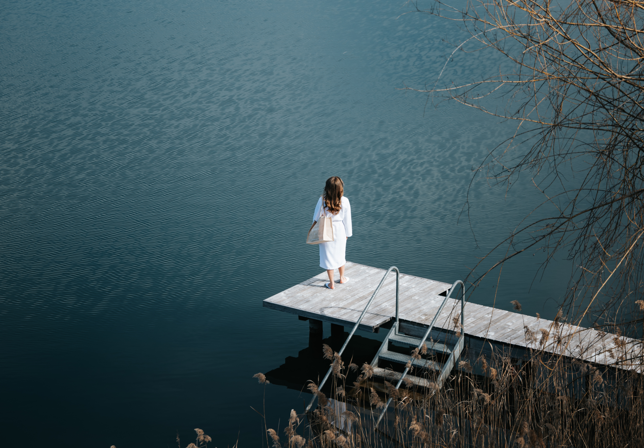 Frau steht auf einem Schiffsanleger und blickt auf einen ruhigen See.